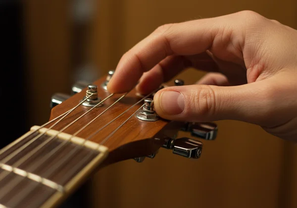 Hand adjusting a guitar tuning peg on a headstock to tune