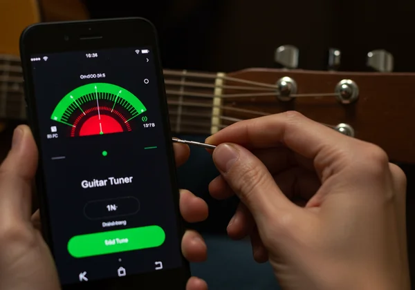 Hand adjusting guitar tuning peg, online tuner display shows pitch