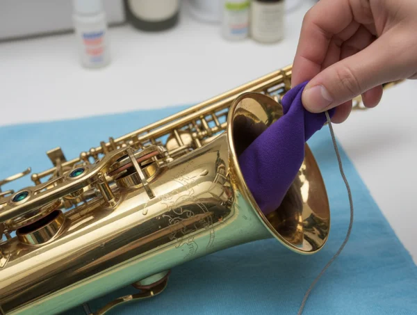 Hand cleaning a saxophone with a cleaning swab